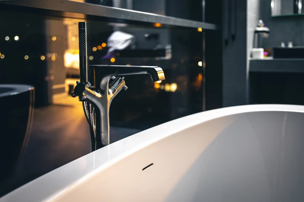 Moderne Armatur über einer freistehenden Badewanne in einem dunkel gehaltenen Badezimmer